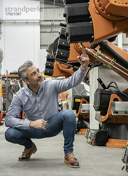 Ingenieur zeigt auf Roboterarm  der in der Fabrik untersucht wird