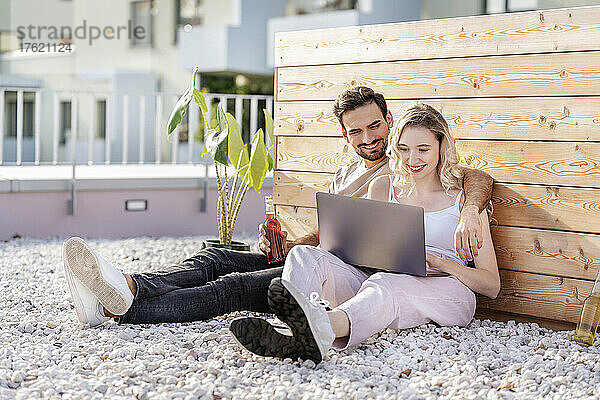 Lächelndes junges Paar  das an einem sonnigen Tag einen Laptop teilt