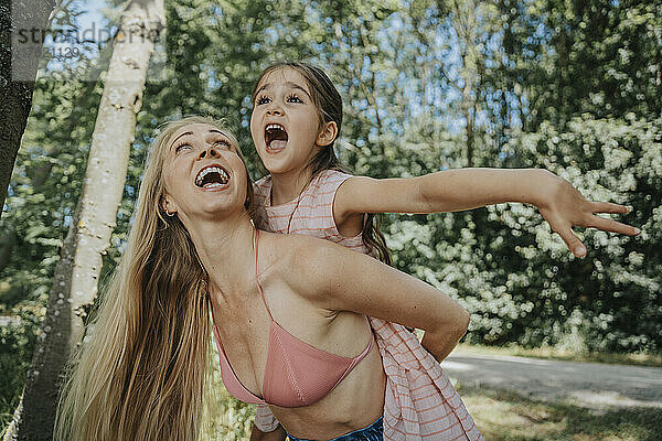 Cheerful mother giving piggyback ride to daughter in nature