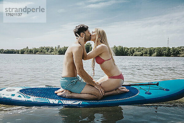 Frau küsst Mann  der auf einem Paddleboard sitzt und über dem See schwimmt