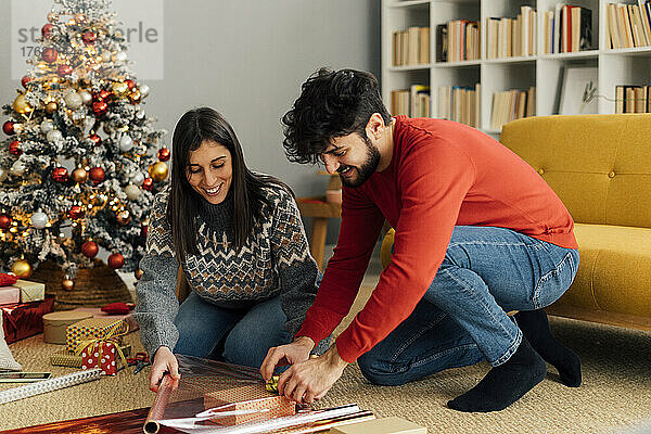 Lächelndes Paar verpackt Weihnachtsgeschenk im heimischen Wohnzimmer