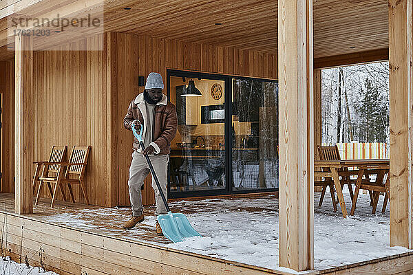 Mann schaufelt im Winter Schnee von der Veranda vor dem Haus