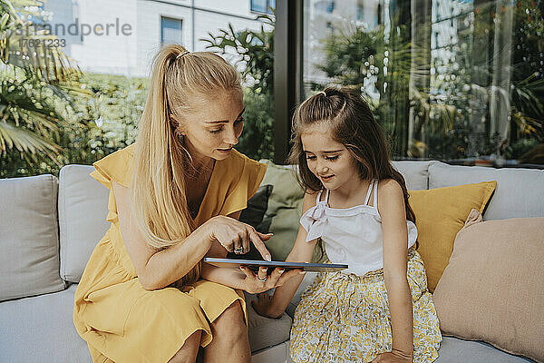 Mutter teilt Tablet-PC mit Tochter  die auf dem Sofa auf der Terrasse sitzt