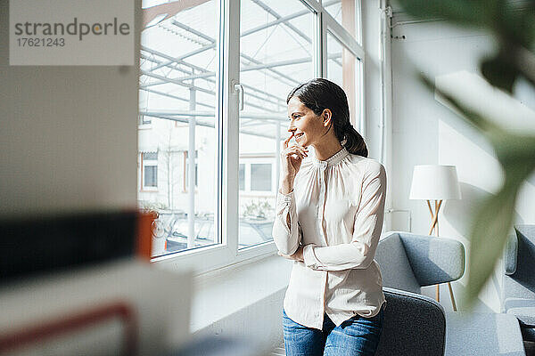 Lächelnde Geschäftsfrau  die durch das Fenster im Büro schaut