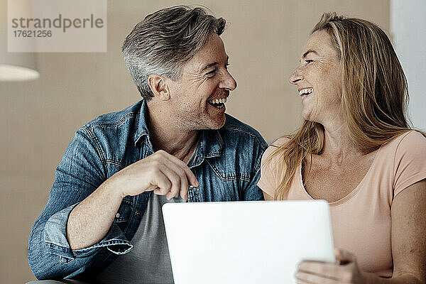 Fröhliche Frau und Mann sitzen zu Hause mit Laptop