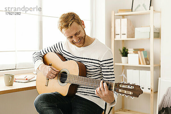 Glücklicher junger Mann  der zu Hause Gitarre spielt