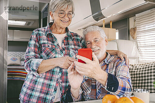 Lächelndes älteres Paar benutzt Smartphone im Wohnmobil