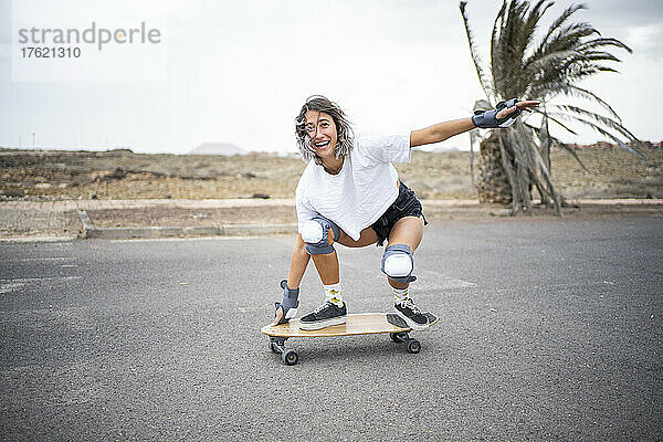 Glückliche junge Frau  die auf der Straße Skateboard fährt