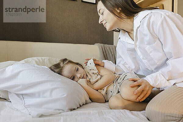 Lächelnde Frau schaut Tochter an  die zu Hause im Bett liegt