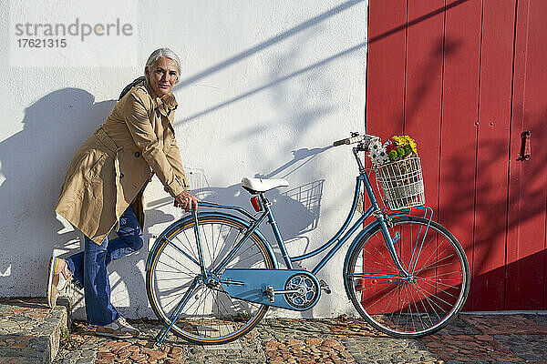 Frau lehnt an einem Fahrrad und steht an einem sonnigen Tag vor einer Wand