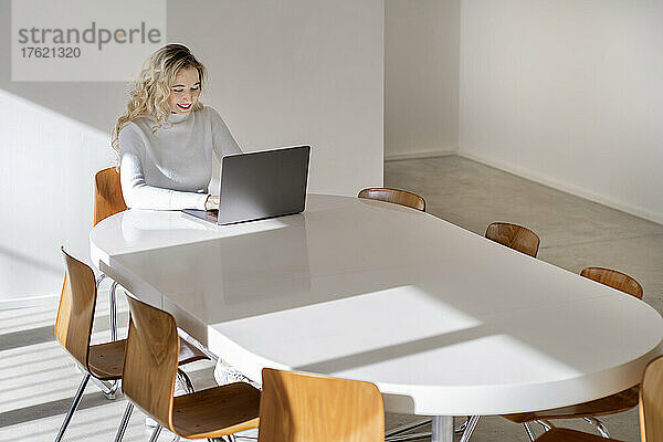 Lächelnde junge Frau mit Laptop am Tisch sitzend