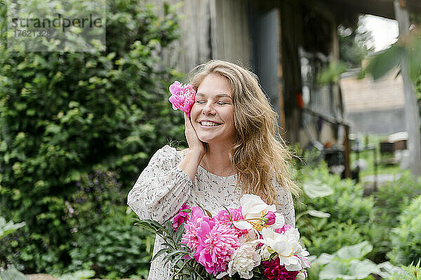 Glückliche blonde Frau mit geschlossenen Augen und rosa Blume im Garten