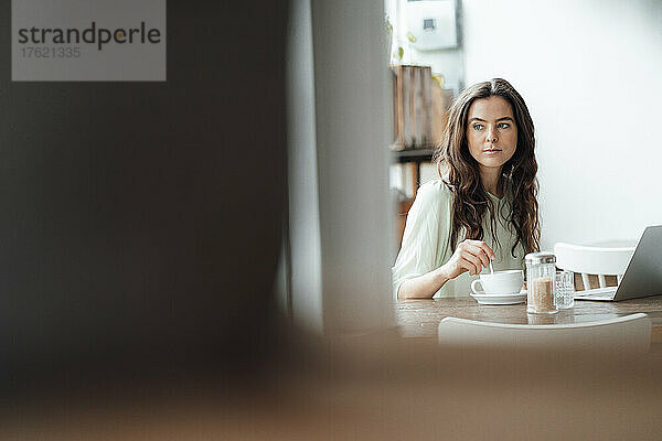 Thoughtful woman mixing coffee in cup on table at cafe