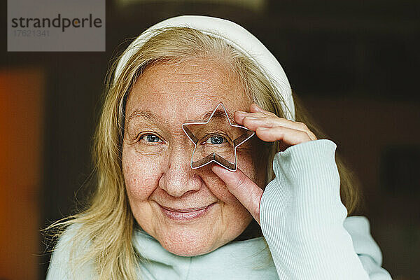 Senior woman looking through star shaped cookie cutter