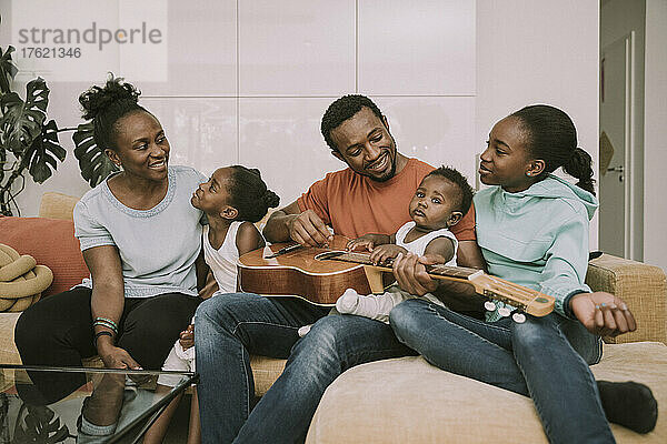 Lächelnder Vater spielt Gitarre mit der Familie im Wohnzimmer
