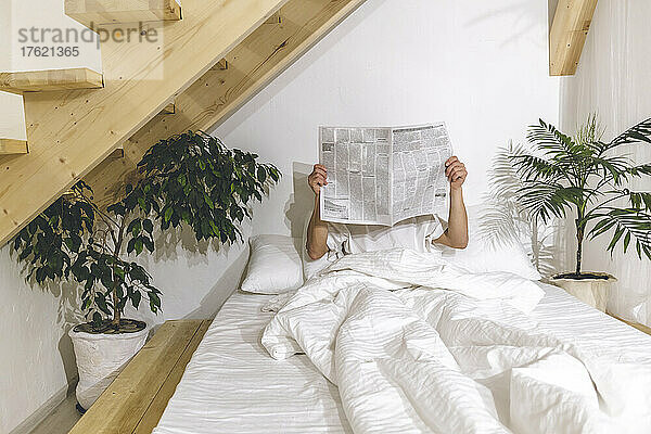 Mann liest Zeitung und sitzt zu Hause im Bett