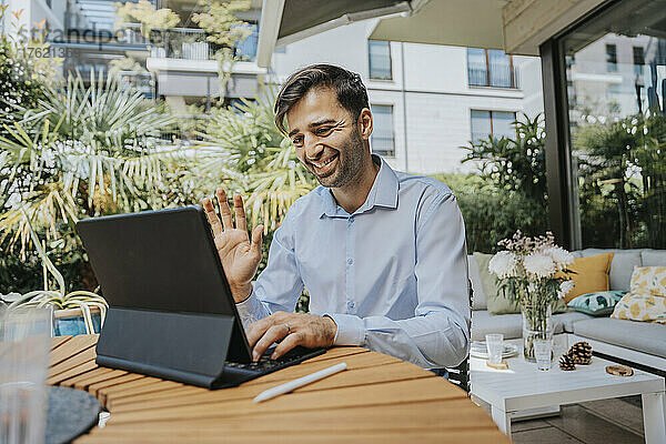 Lächelnder Geschäftsmann winkt bei Videoanruf über Tablet-PC im Hinterhof