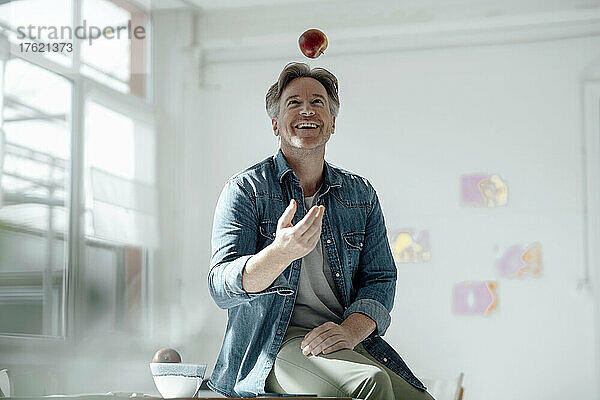 Smiling man throwing apple sitting on table