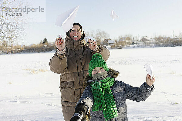 Glückliche Mutter und Sohn spielen mit Papierflieger im Schnee