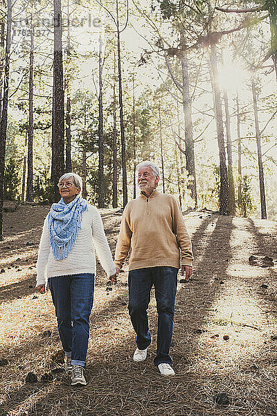 Glückliches älteres Paar in warmer Kleidung  das gemeinsam im Wald spaziert