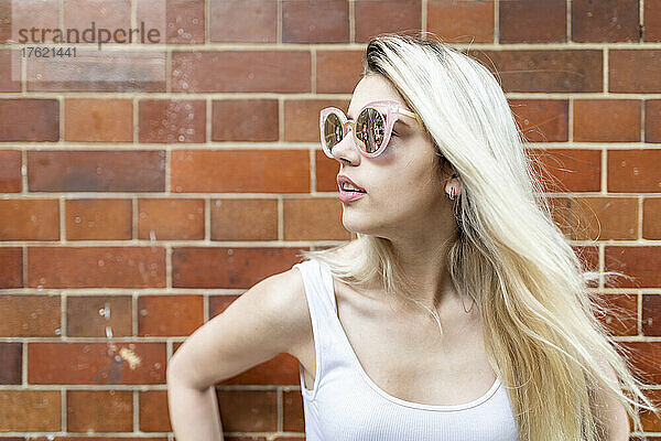 Teenage girl wearing sunglasses standing in front of brick wall