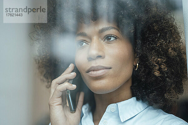 Berufstätige Frau mit lockigem braunem Haar  die auf dem Smartphone spricht