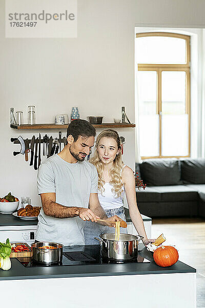 Blonde Frau unterhält sich mit ihrem Freund und bereitet zu Hause in der Küche Pasta zu
