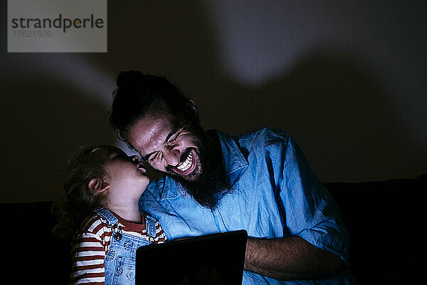 Sohn flüstert dem glücklichen Vater zu Hause vor dem Tablet-PC ins Ohr