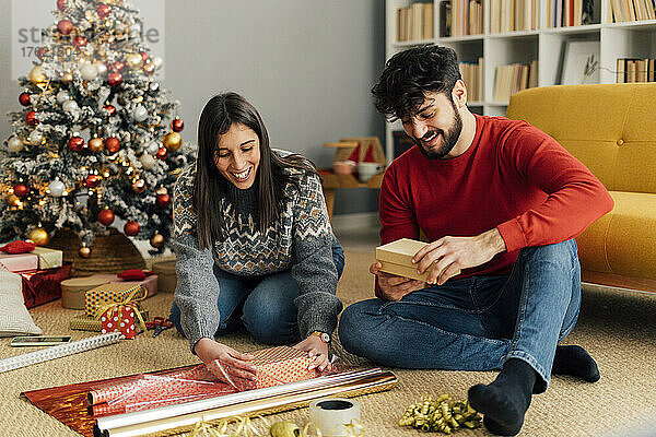 Glückliches Paar packt Weihnachtsgeschenk ein und sitzt vor dem Sofa