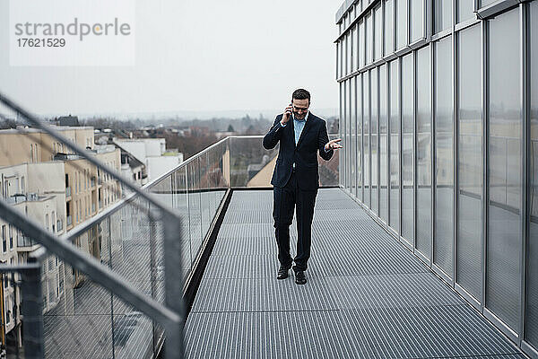 Glücklicher Geschäftsmann  der auf dem Balkon mit dem Handy spricht