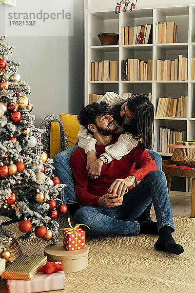 Frau umarmt Freund zu Hause am Weihnachtsbaum