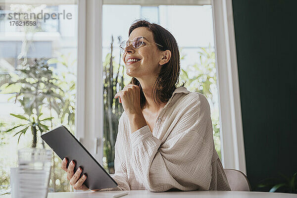 Glückliche Frau sitzt zu Hause mit Tablet-PC