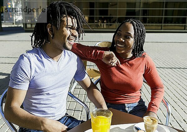 Lächelndes Paar sitzt an einem sonnigen Tag im Straßencafé