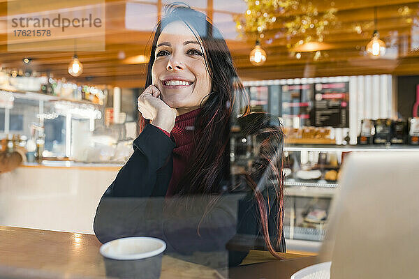 Nachdenkliche Geschäftsfrau mit der Hand am Kinn  gesehen durch ein Glas Café