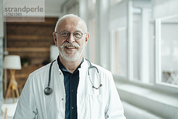 Lächelnder Arzt mit Stethoskop und Brille im Krankenhaus