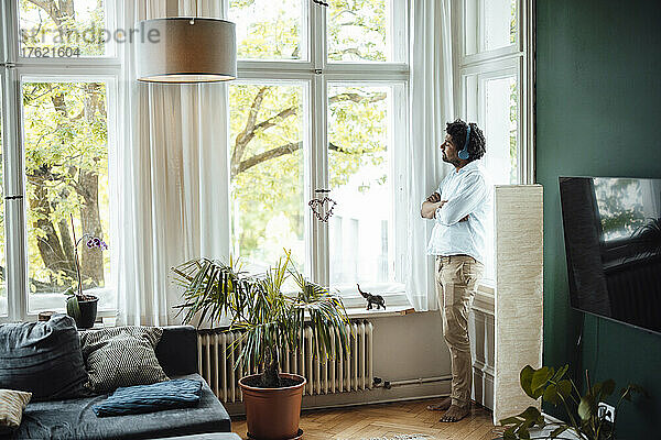 Mann hört Musik über kabellose Kopfhörer und schaut zu Hause durch das Glasfenster