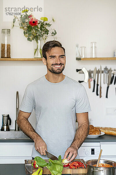 Smiling handsome man chopping food in kitchen at home