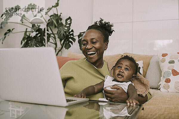 Cheerful mother using laptop holding son in living room