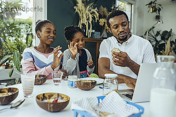 Vater und Töchter per Videoanruf über Laptop am Frühstückstisch
