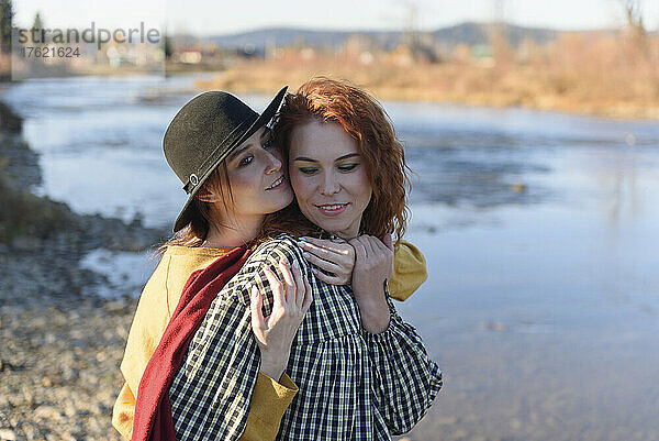 Lächelnde Frau umarmt ihre Freundin am Wochenende am Fluss