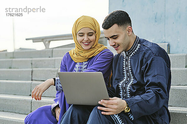 Junger Mann benutzt Laptop und sitzt mit Frau auf der Treppe