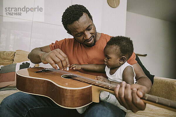 Vater zeigt seinem kleinen Jungen im Wohnzimmer Gitarre