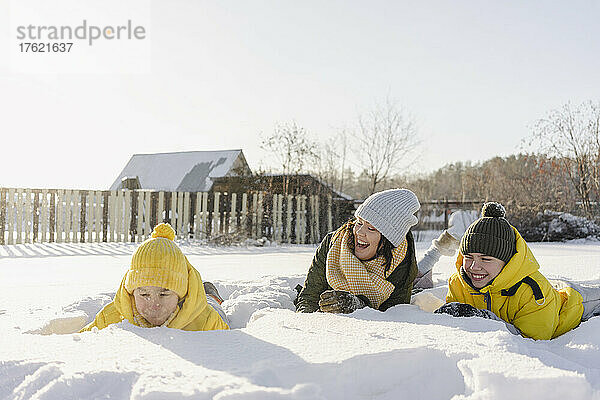 Verspielte Jungen mit Mutter  die im Winter auf Schnee liegen