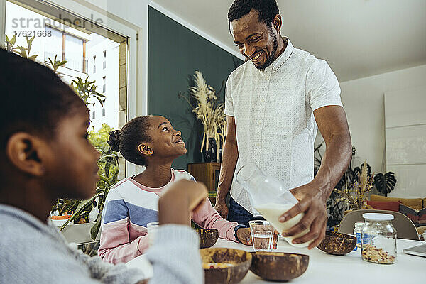 Lächelnder Vater schenkt seiner Tochter am Tisch Milch ein