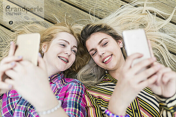 Happy teenagers taking selfie through smart phone lying on floorboard