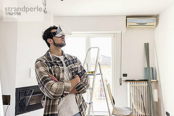 Mann mit verschränkten Armen und VR-Brille blickt auf Hausrenovierung