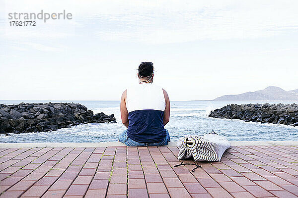 Mann sitzt auf der Promenade und blickt aufs Meer