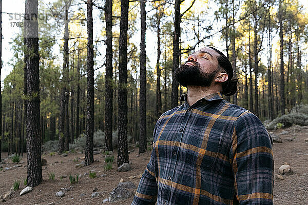 Bärtiger Mann mit geschlossenen Augen steht im Wald