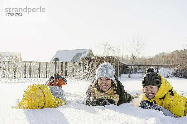 Fröhliche Jungen mit Mutter  die im Winter auf Schnee liegen
