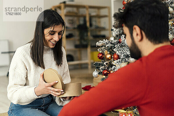 Lächelnde Frau öffnet Geschenk vor ihrem Freund zu Hause